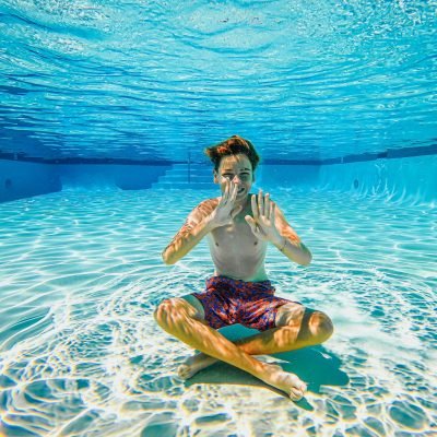 Boy having fun sitting underwater in a sunlit swimming pool.
